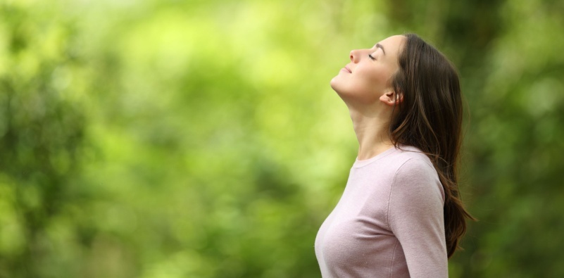 A woman outside, standing with her eyes closed and head pointed upwards