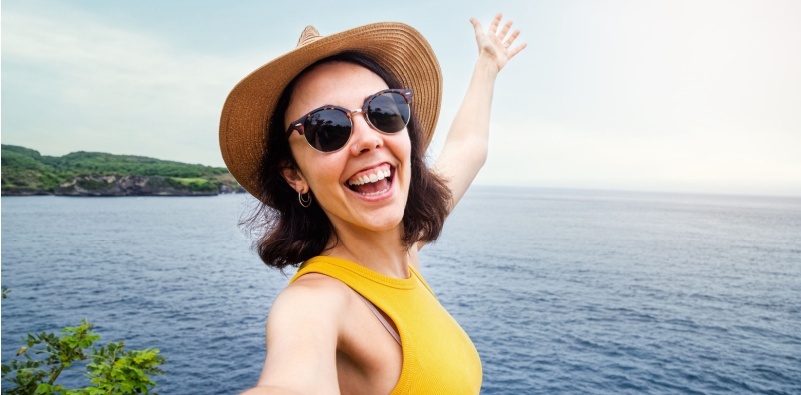 A woman wearing a hat and sunglasses enjoying being by the sea.]