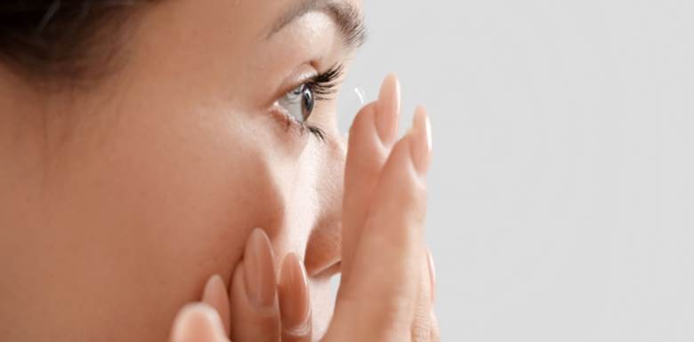 Young woman putting in contact lenses on a light background, closeup