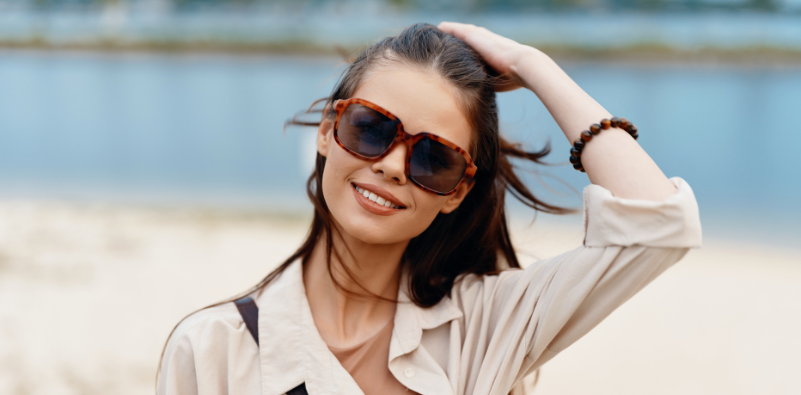 A woman by the water wearing a pair of tortoiseshell sunglasses.
