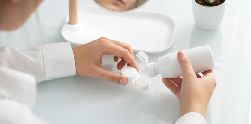 A young person adding solution to their contact lens case, in a clean environment