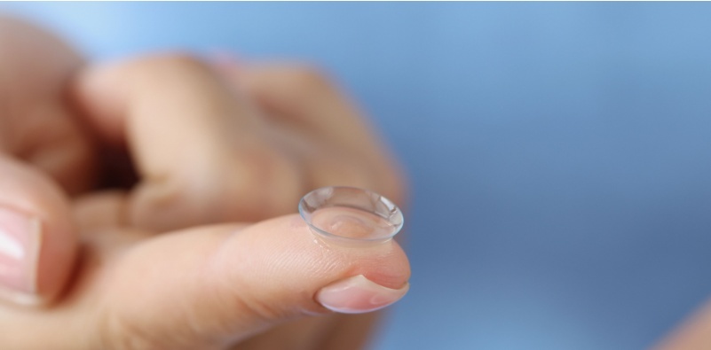A close-up of a female hand, with a contact lens on the tip of their index finger