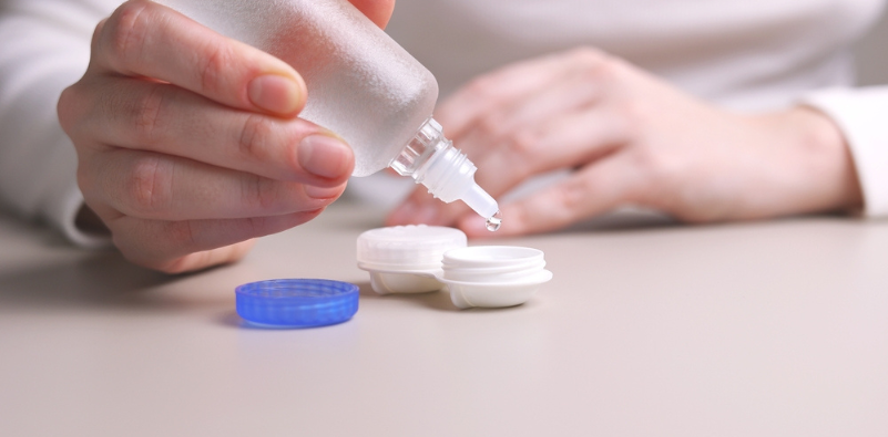 A close-up of a person putting contact lens solution in their contact lens storage pot.
