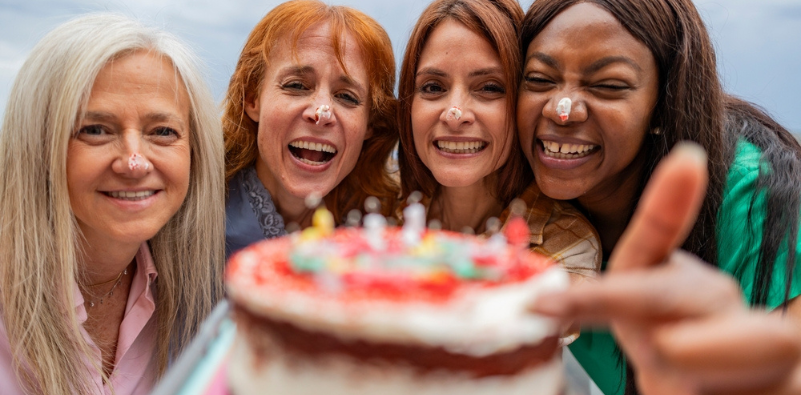 A group of middle-aged women laughing, with icing from a birthday cake on their noses.