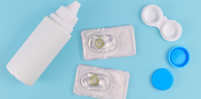 Two packets of hazel coloured contact lenses, a contact lens storage container and cleaning solution on a blue background.]