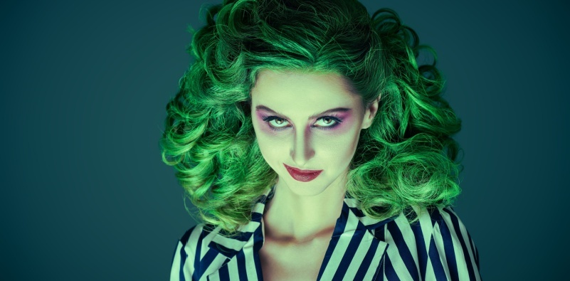 A young woman in a Halloween costume with green hair and violet eye make-up dressed in a striped suit.