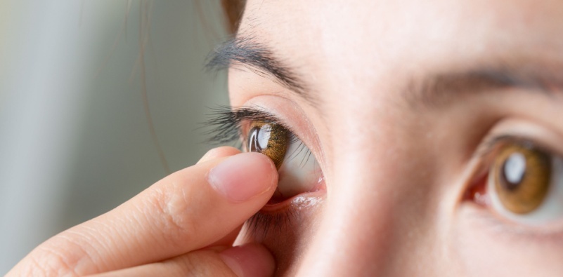 A close-up of a woman removing a contact lens from her eye