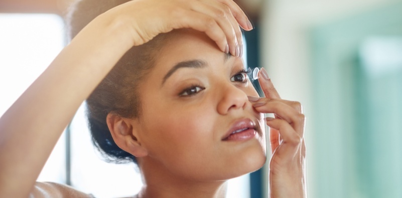 A young woman with a contact lens on her finger, about to insert it in her eye