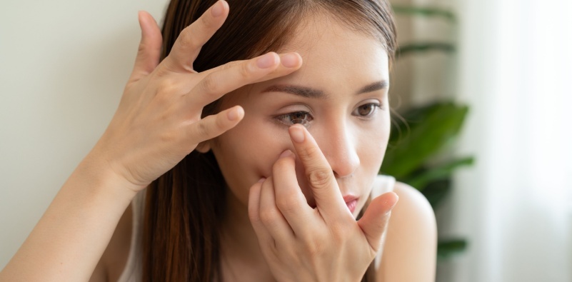 A young woman holding her eye open, ready to insert a contact lens