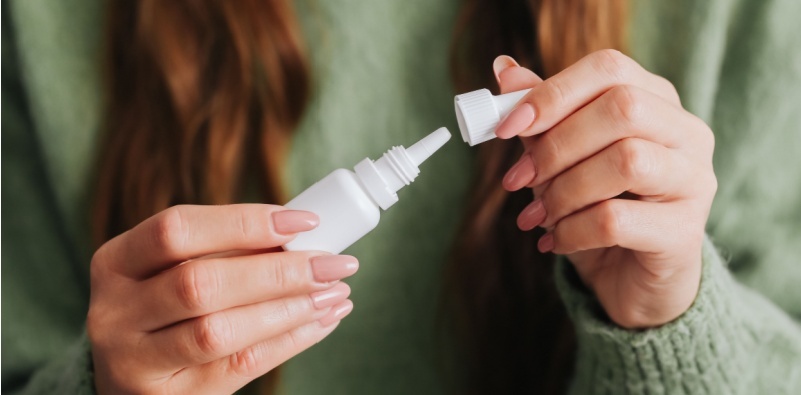 A woman in a green jumper, opening a bottle of eye drops