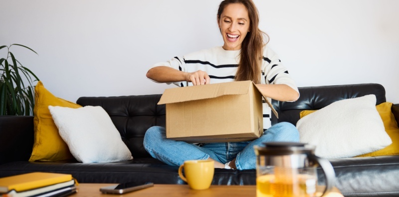 A woman opening a parcel that has been delivered on their sofa