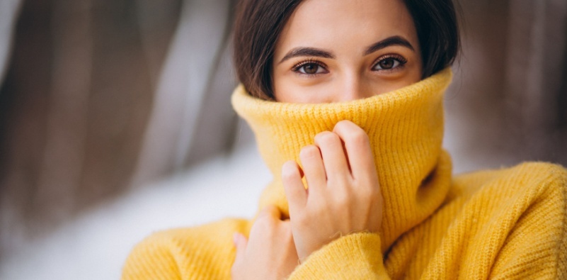 A portrait of a young woman with a yellow turtleneck jumper pulled up to her nose.