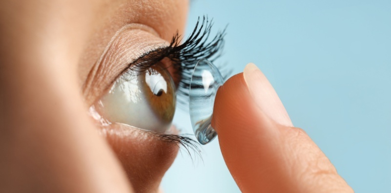 A close up of a young woman putting a contact lens in her eye.