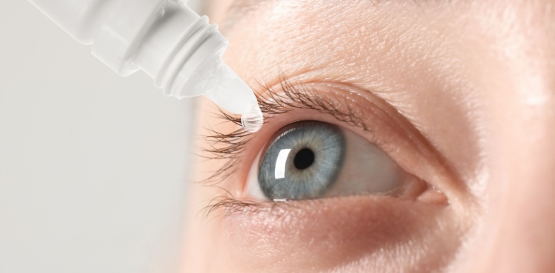 A close up of a person putting eye drops in their blue eye.