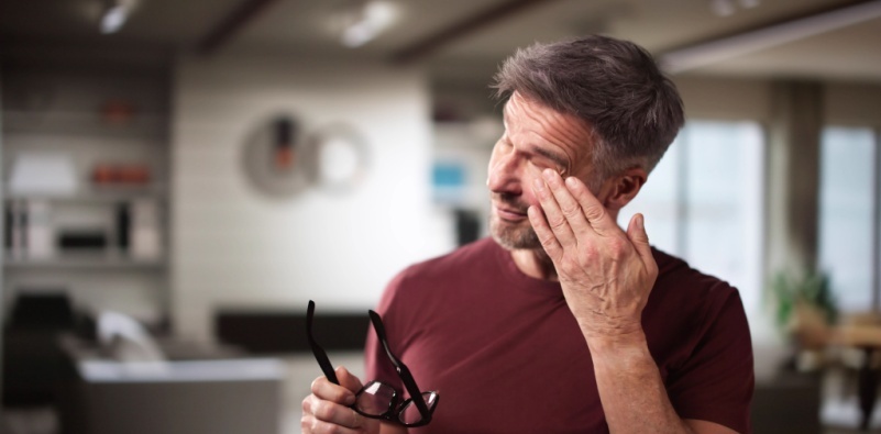 A middle aged man holding his glasses in one hand, rubbing his eye with the other.