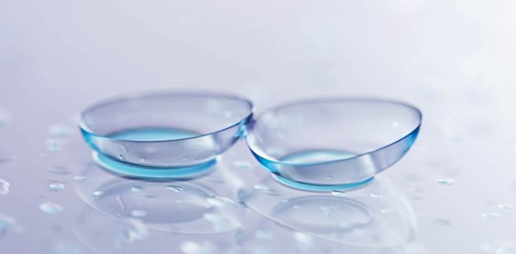 A pair of contact lenses and water drops on light mirror surface, closeup.