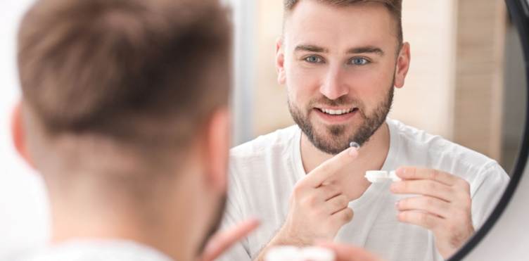 Young man putting in contact lenses near mirror.