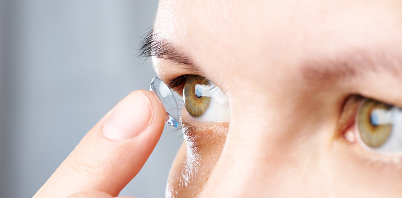 A close up of a person with a contact lens on the tip of their finger about to insert it in their eye.