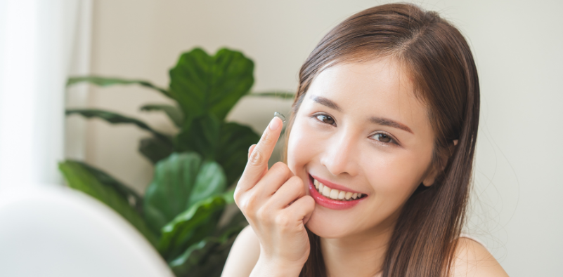 A woman holding a contact lens near her eye and smiling.