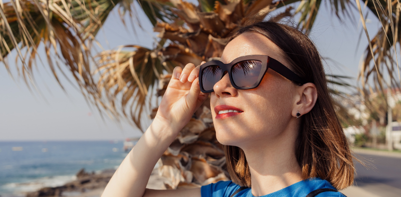A woman wearing a pair of oversized, brown sunglasses at the beach.