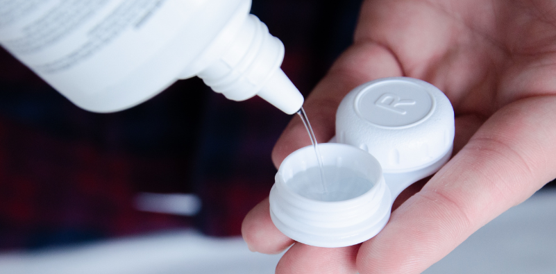 Person holding a contact lens storage case while pouring contact lens solution into it