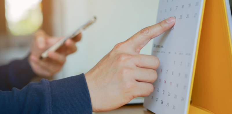 A man pointing to a calendar while holding a mobile phone